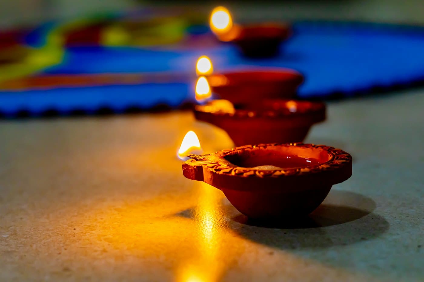Lit terracotta diyas lined on stone, with a coloured floor pattern behind them